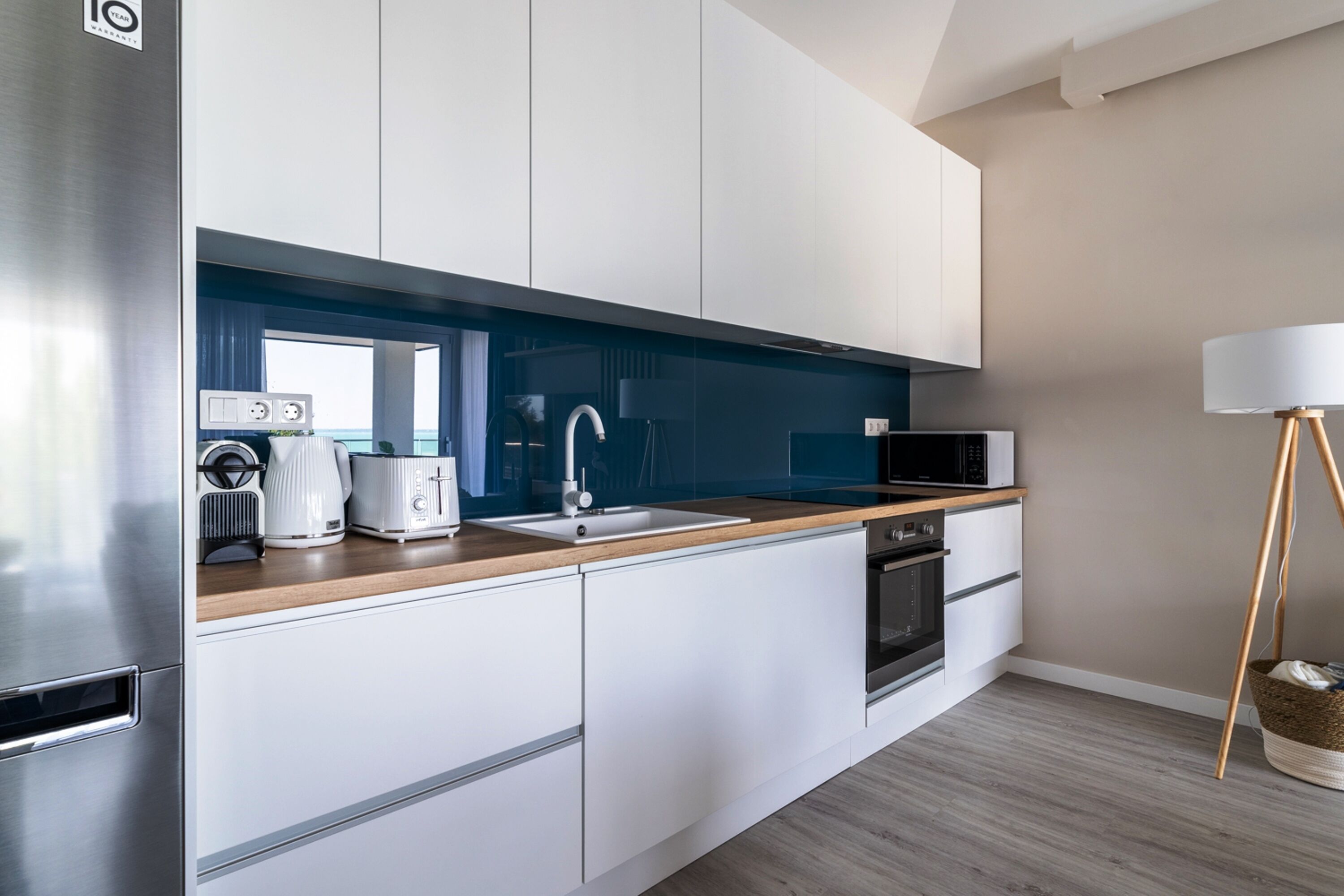 A modern kitchen with white cabinets, a wooden countertop, a sink, a microwave, and a stove.