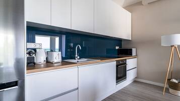 A modern kitchen with white cabinets, a wooden countertop, a sink, a microwave, and a stove.