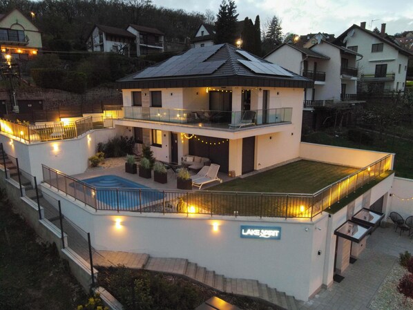 A modern two-story house with a swimming pool, outdoor seating, and a sign reading "LAKE SPIRIT".