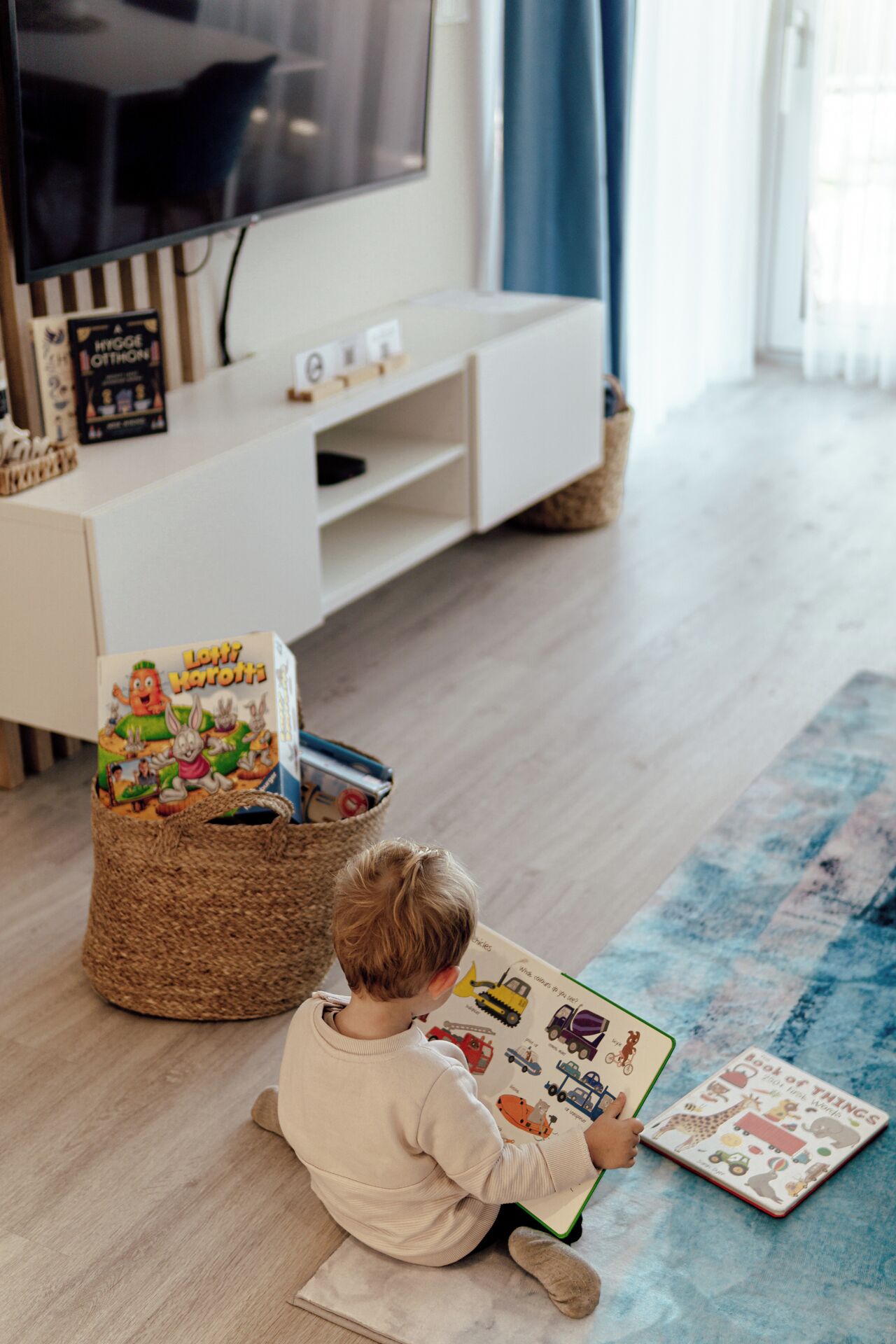 Ein Kind liest ein Buch in einem Raum mit Fernseher, Bücherregal und einem gewebten Korb.