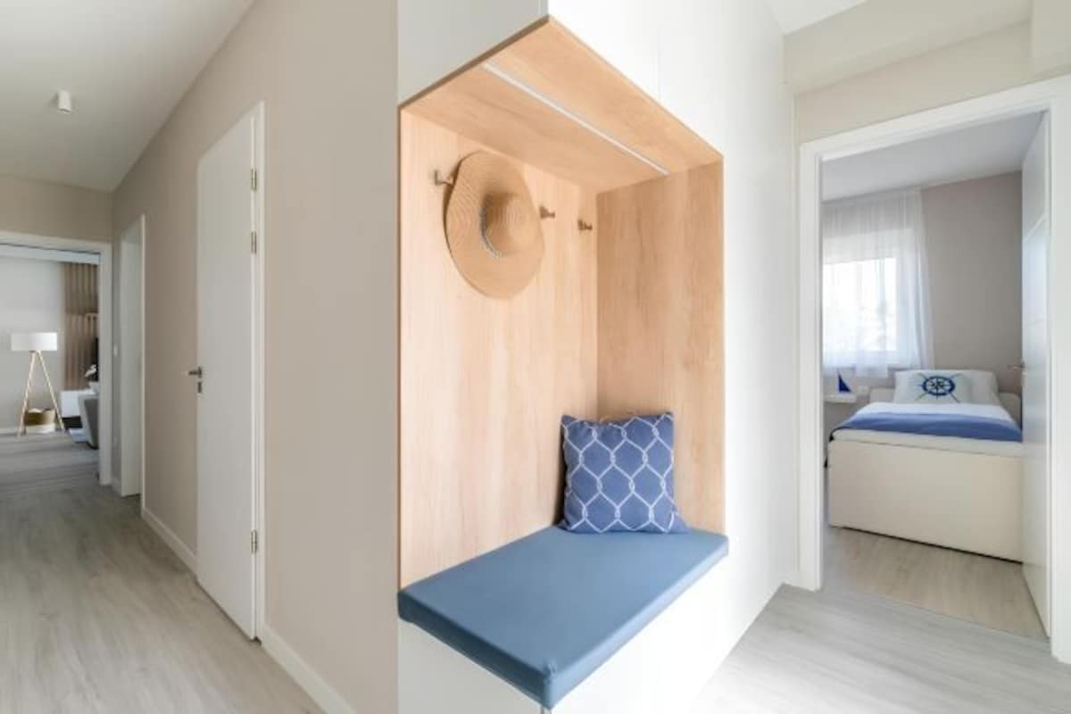 Ett modernt hotellrum med en inbyggd bänk, en säng med ett blått och vitt överkast och en vägg med träpanel som ger rummet en accentfärg.
