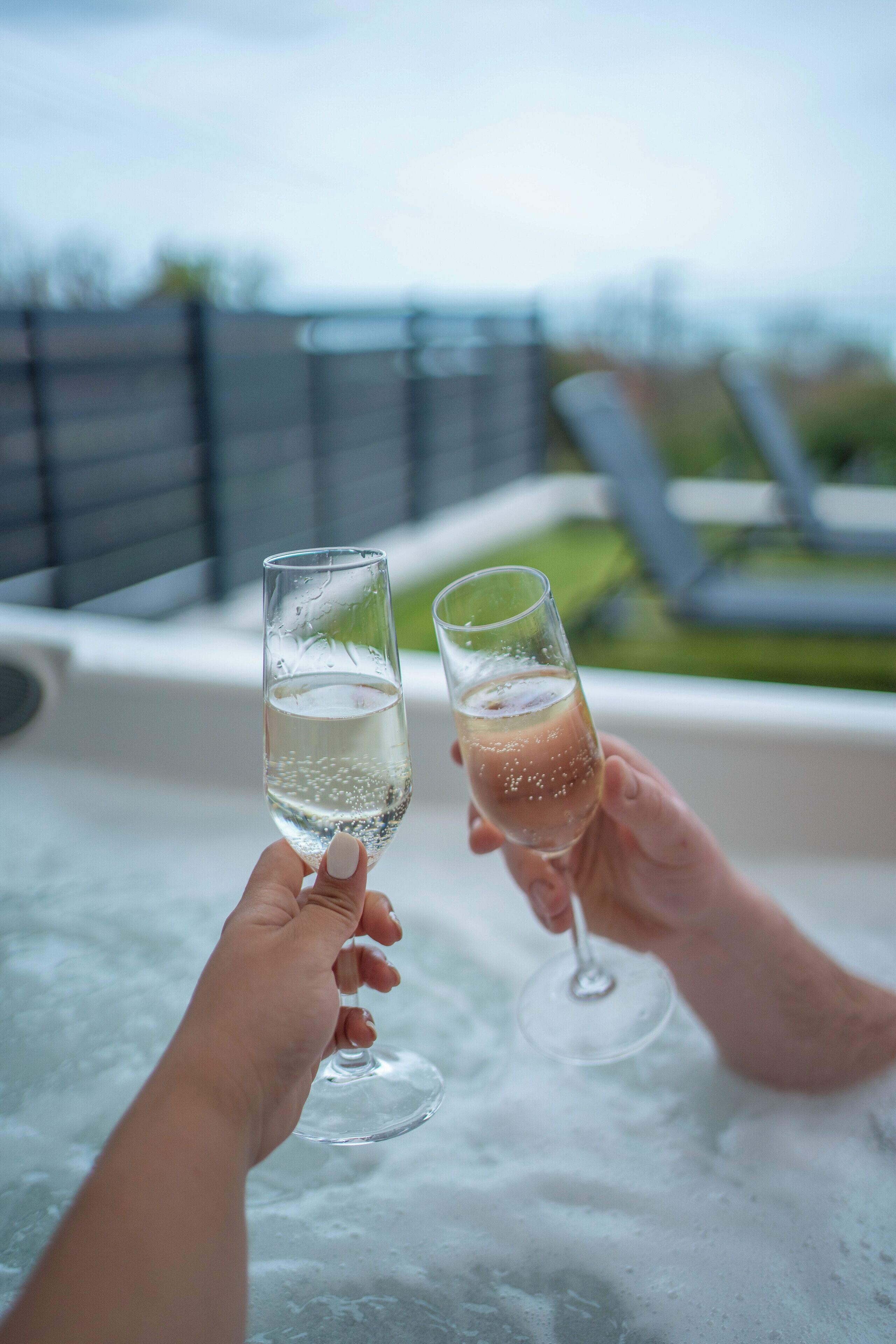 Two people holding champagne glasses over a hot tub.