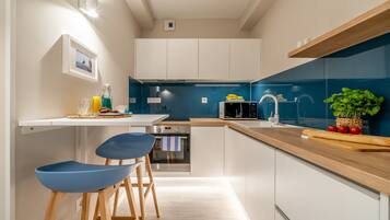 Una cocina moderna con armarios blancos, salpicadero azul y encimeras de madera. Hay dos taburetes de bar azules y un microondas.
