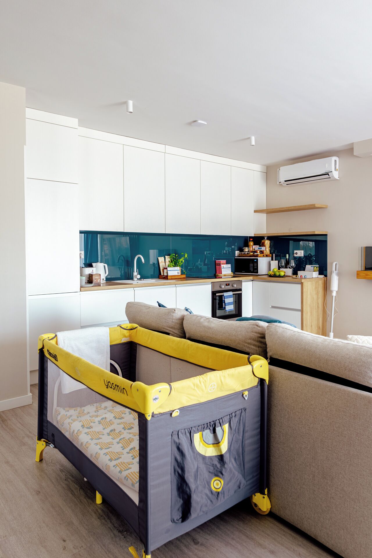 A modern living space with a convertible playpen, a kitchen area, and a sofa.