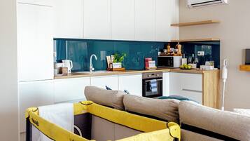 A modern living space with a convertible playpen, a kitchen area, and a sofa.