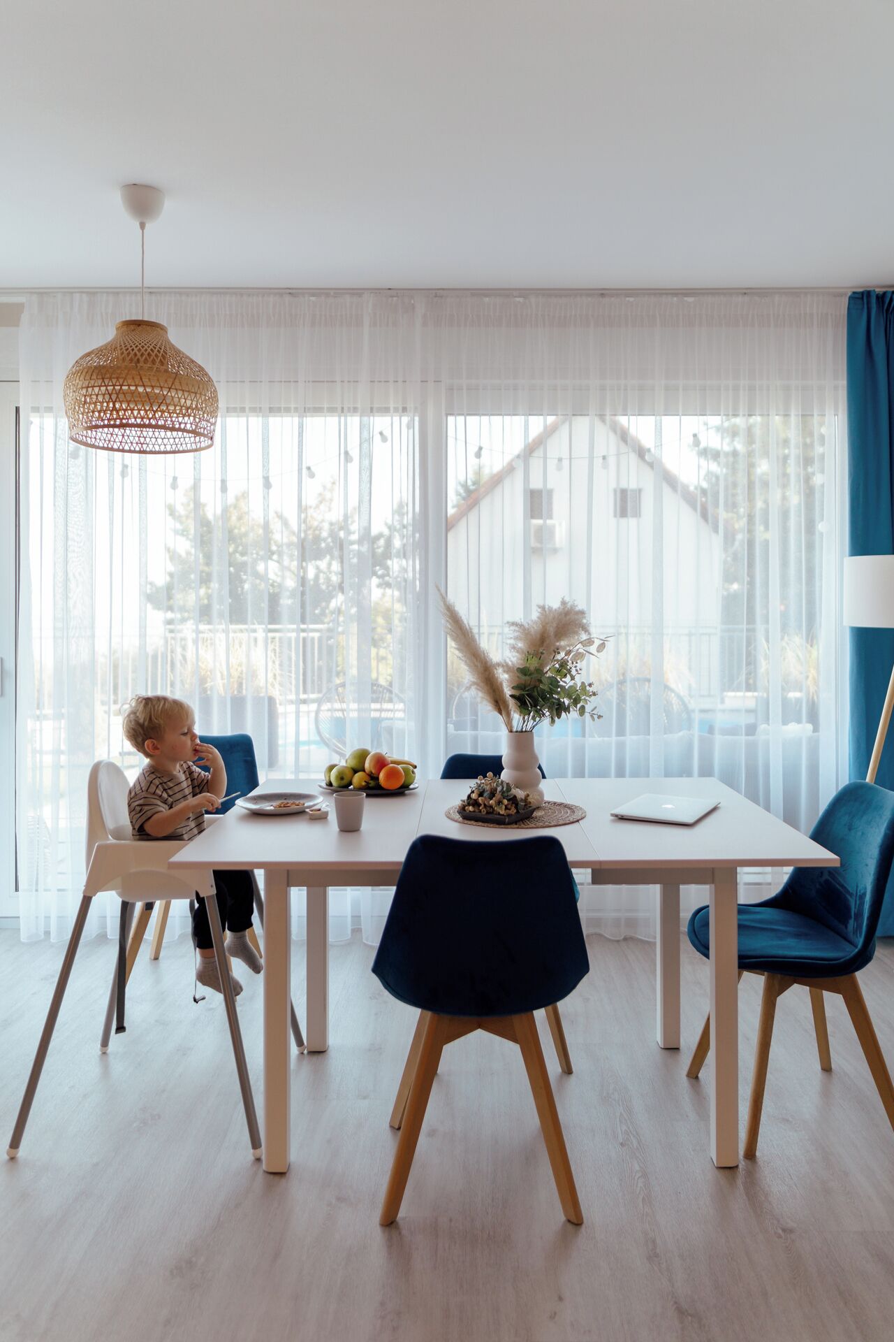 A modern dining area with a white table, blue chairs, and a child seated.