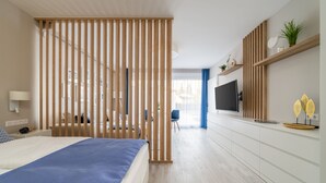 A modern hotel room with a bed, a desk, a TV, and a view of the city. - Lake Spirit Boutique Apartments (Balatonalmadi)