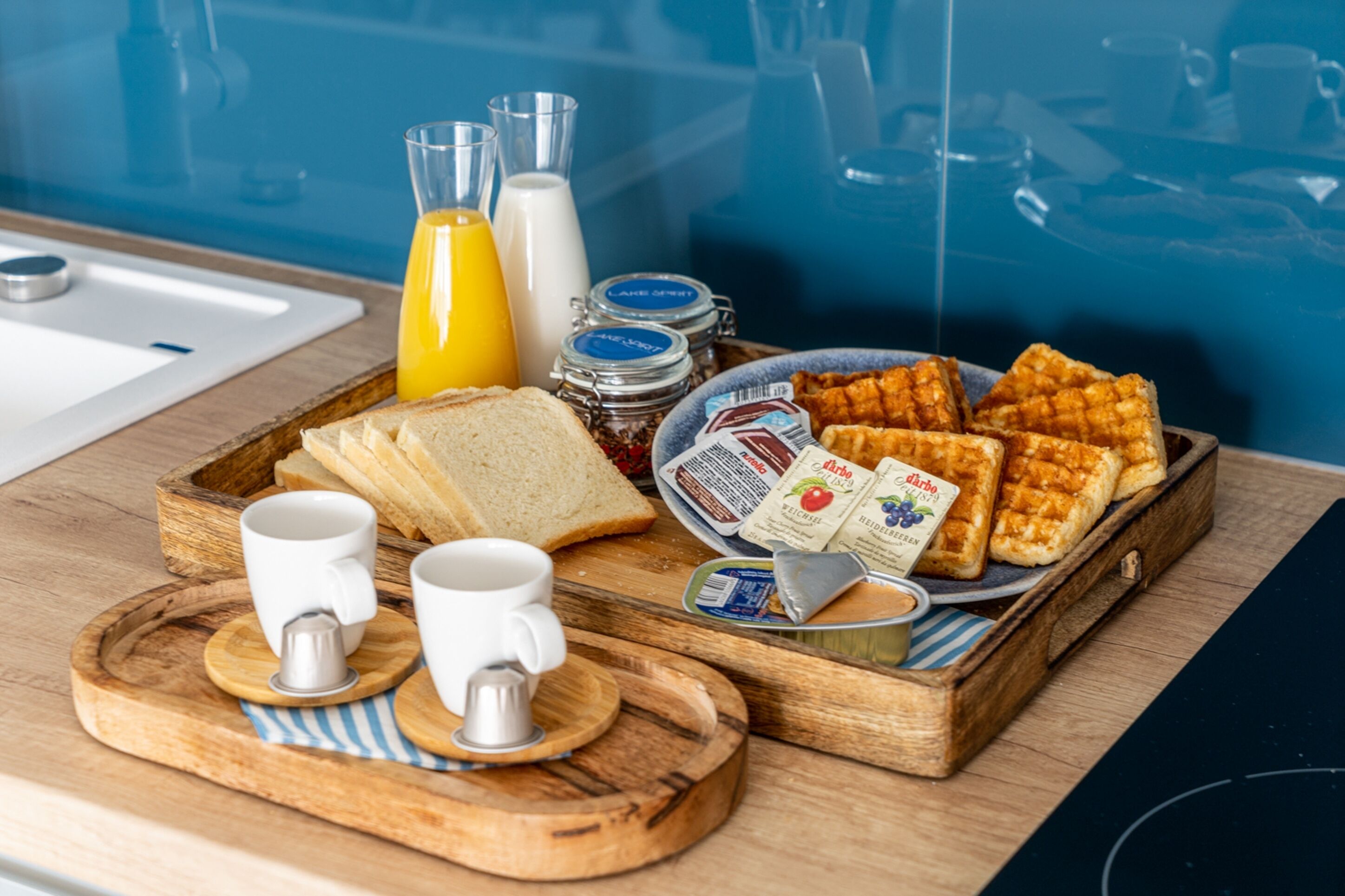 A breakfast tray with waffles, toast, juice, milk, and condiments on a wooden tray.