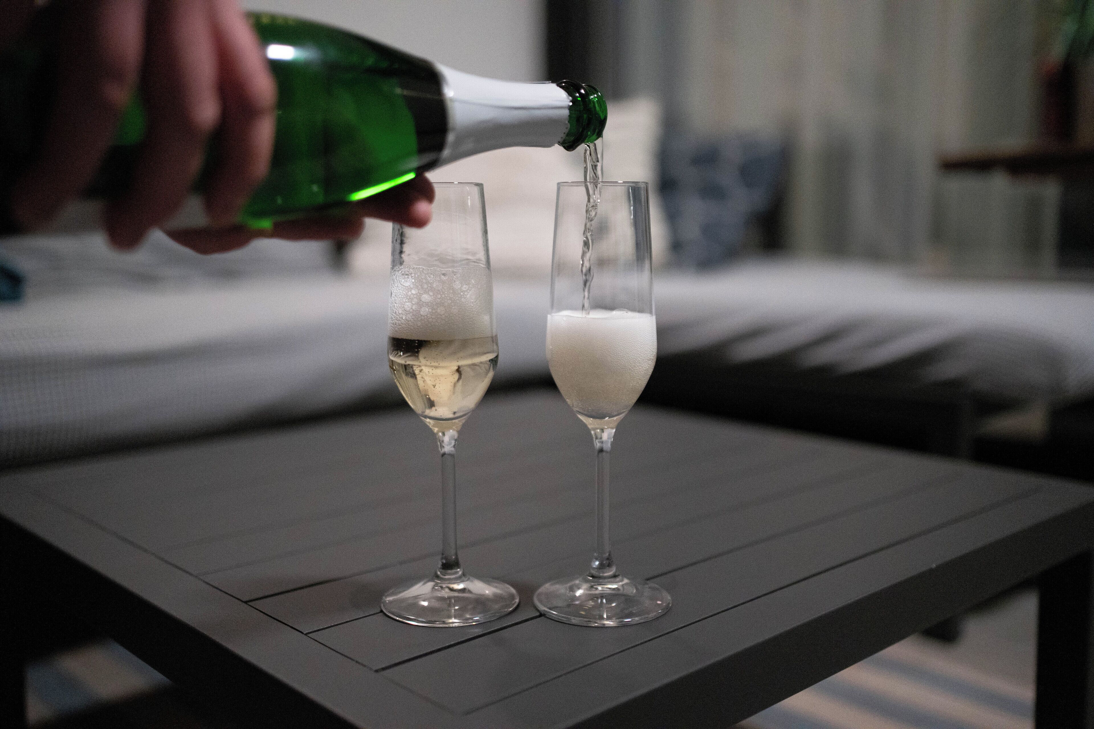 Zwei Gläser auf einem Tisch, eine Flasche gießt Flüssigkeit in eines davon.
