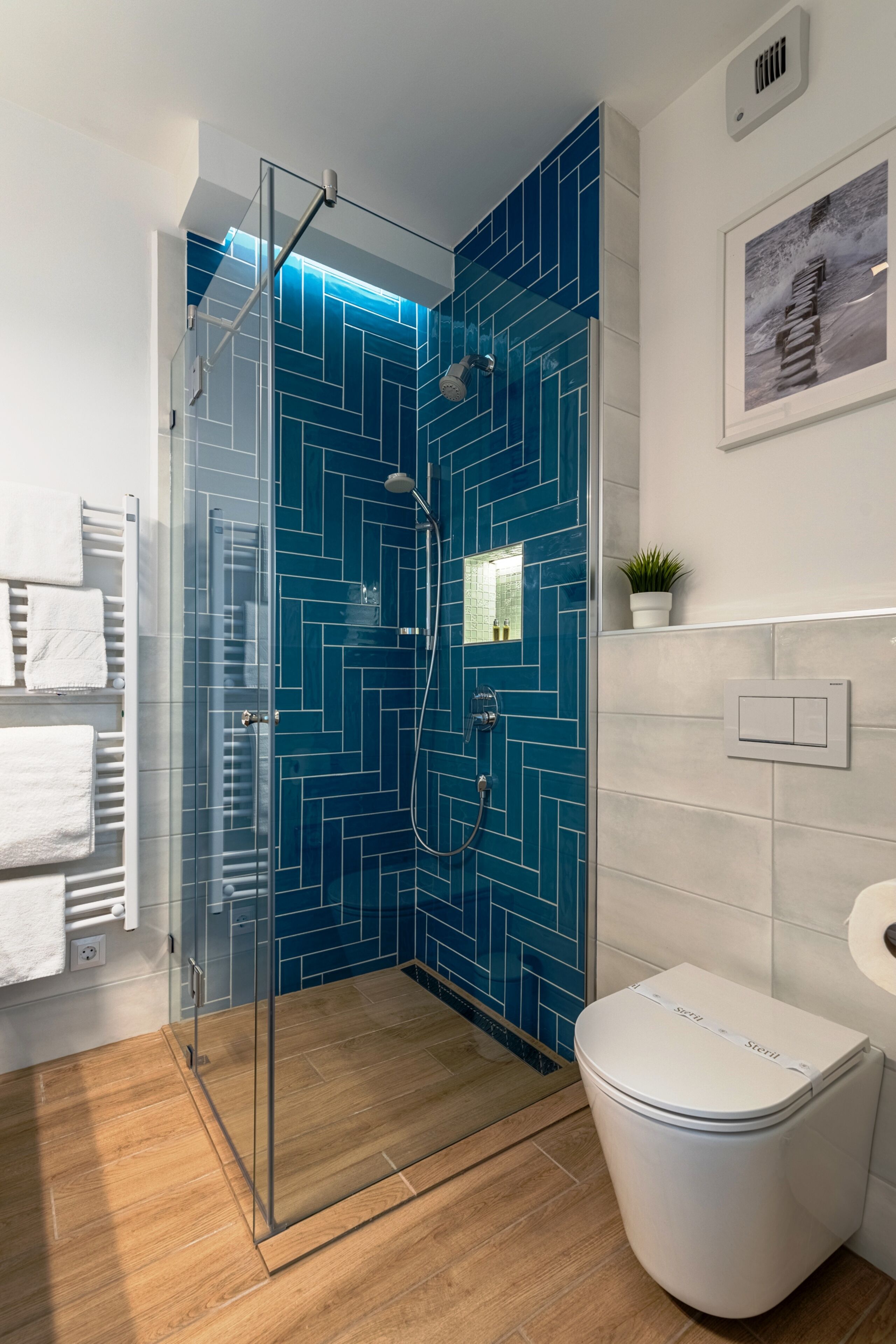 A modern bathroom with a glass-enclosed shower, a white toilet, and a blue tiled wall.