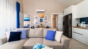 A modern living room with a sofa, a dining table with chairs, a kitchen area with a refrigerator, and a hanging light fixture. - Lake Spirit Boutique Apartments (Balatonalmadi)