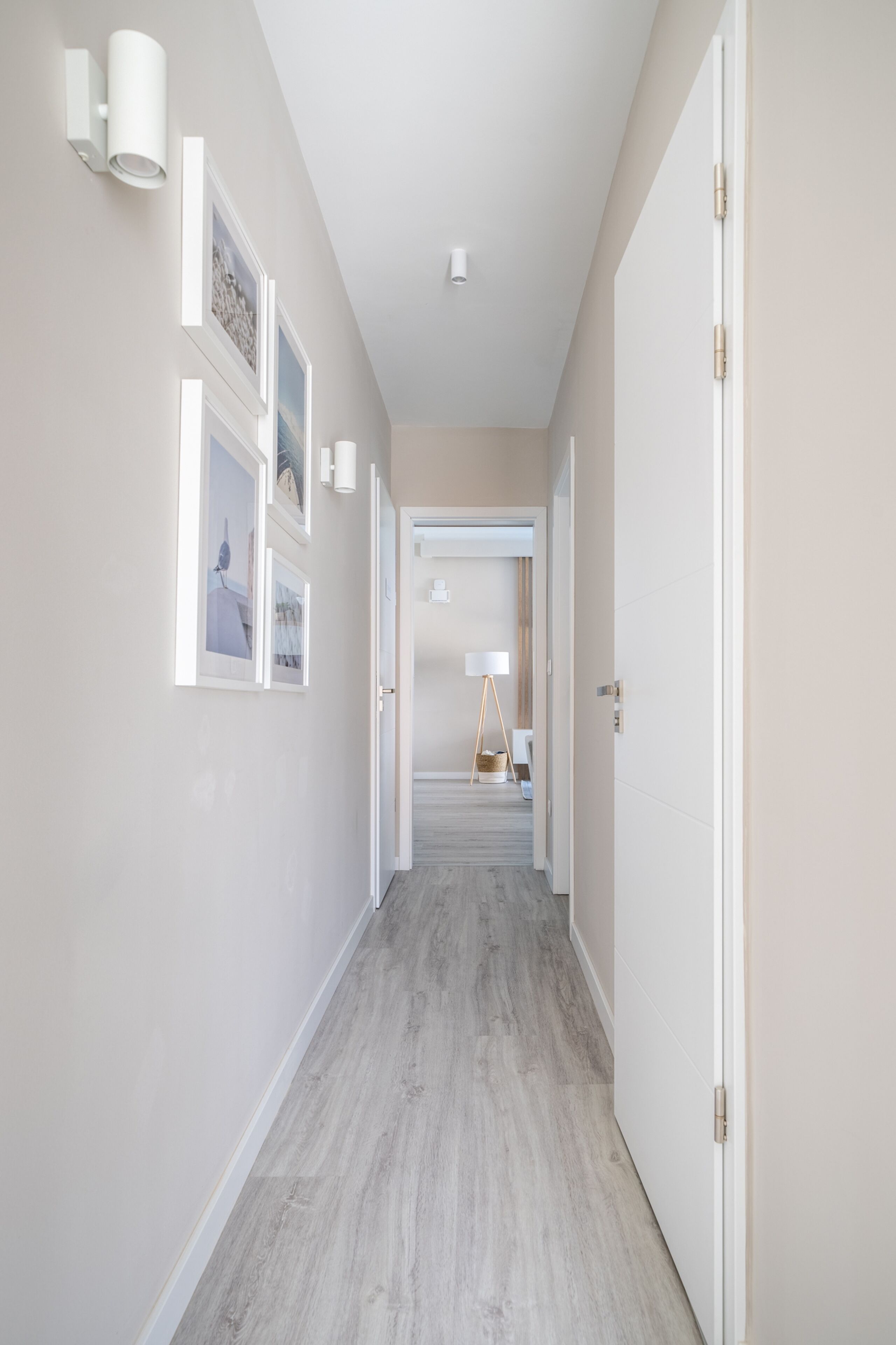 Un pasillo con paredes de tonos claros y suelo de madera, que conduce a una habitación con una cama y una mesita de noche.