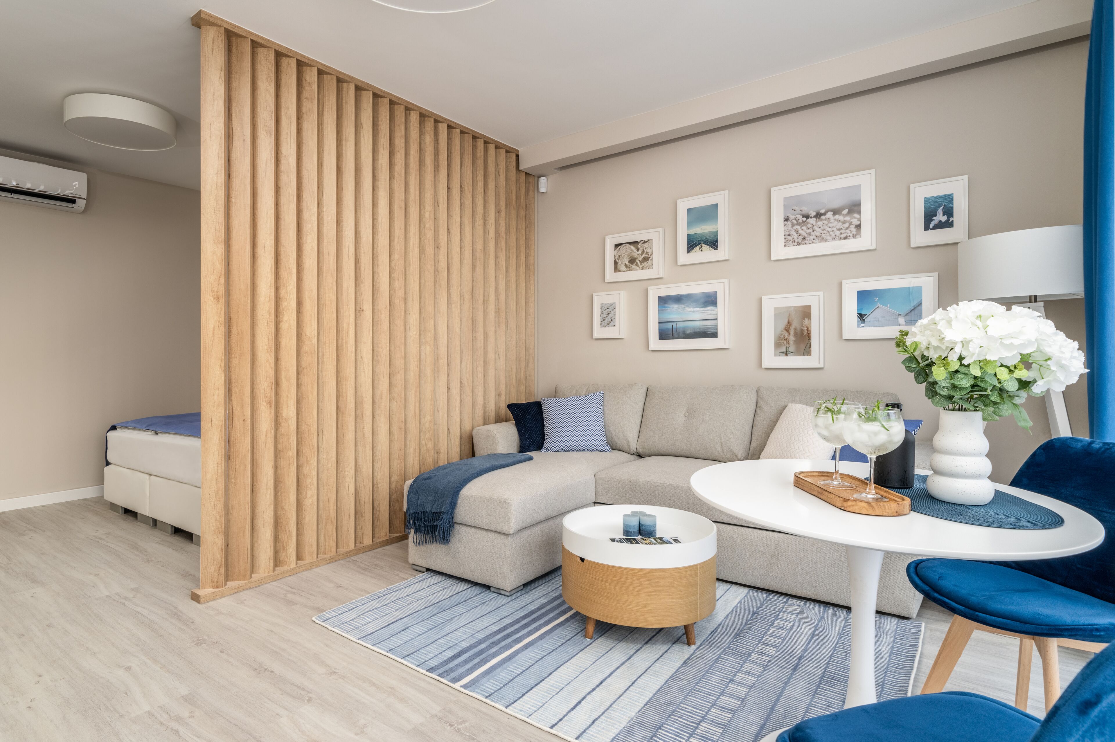 A modern living room with a sectional sofa, a round coffee table, and a blue chair. There are framed pictures on the wall and a potted plant on the table.