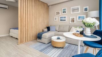 A modern living room with a sectional sofa, a round coffee table, and a blue chair. There are framed pictures on the wall and a potted plant on the table.