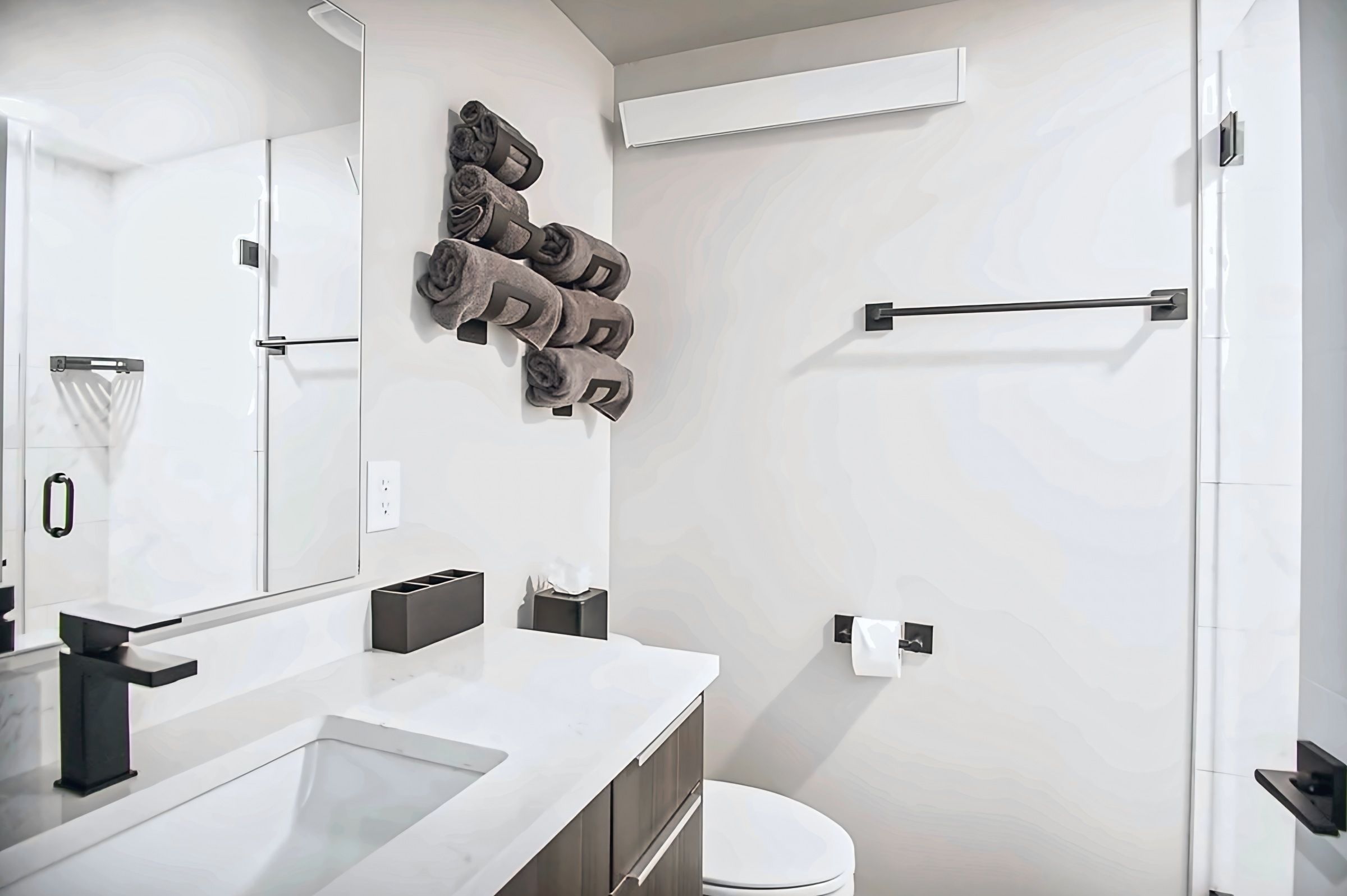 A modern bathroom with a large mirror, a towel rack, a toilet, and a sink with a faucet.