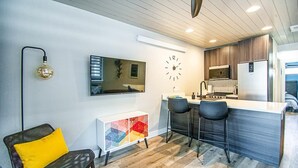 A modern kitchen with a clock, bar stools, and a dining area with a sofa and a colorful cabinet. - Brooklyn Circle Loft — Newly Built 1BR + Loft, Hilltop, Walk Downtown (Leadville)