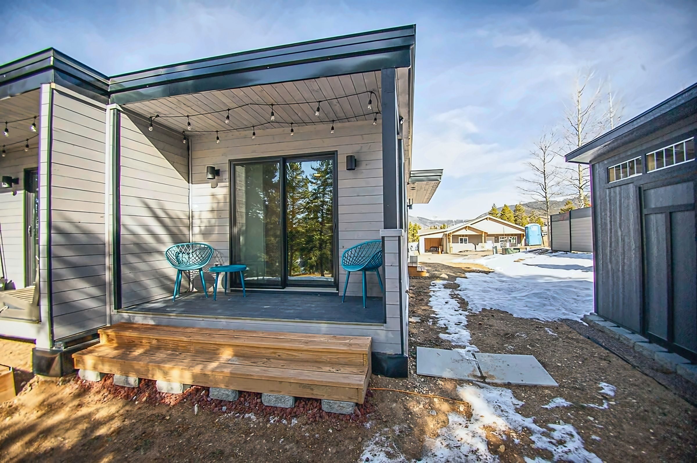 A modern, single-story building with a covered porch, two chairs, and a wooden bench.