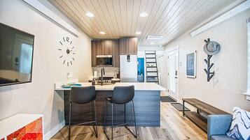 A modern kitchen with a central island, two bar stools, a clock, and a wall-mounted hat rack.
