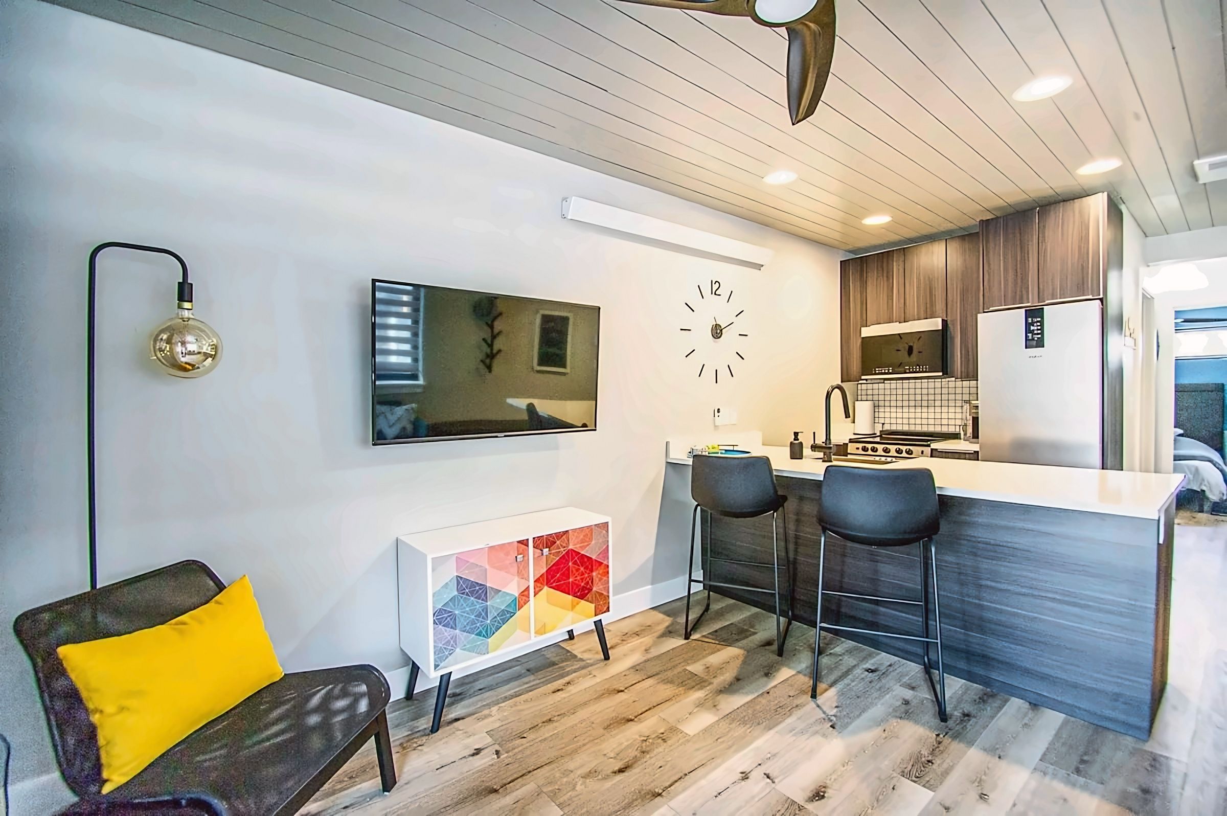 A modern kitchen with a built-in refrigerator, a clock, and a bar area with stools.