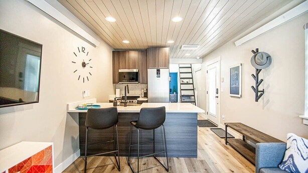 A modern kitchen with a central island, bar stools, a clock, and a minimalist design. - Brooklyn Circle Loft — Newly Built 1BR + Loft, Hilltop, Walk Downtown (Leadville)