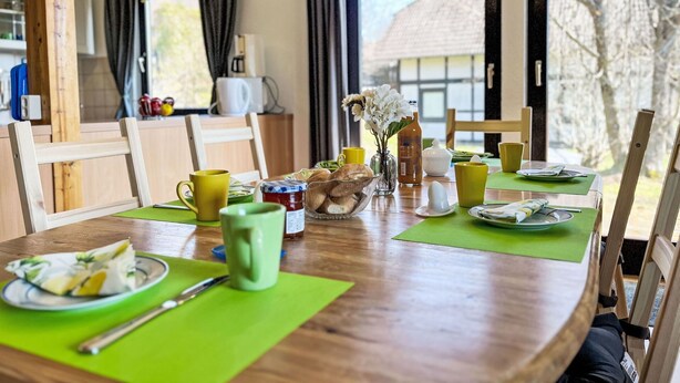 A dining area with a wooden table set for breakfast, including plates, cups, and a vase with flowers. - Beautiful apartment in villa for 4 guests with WIFI, TV and pets allowed (Bad Wildungen)