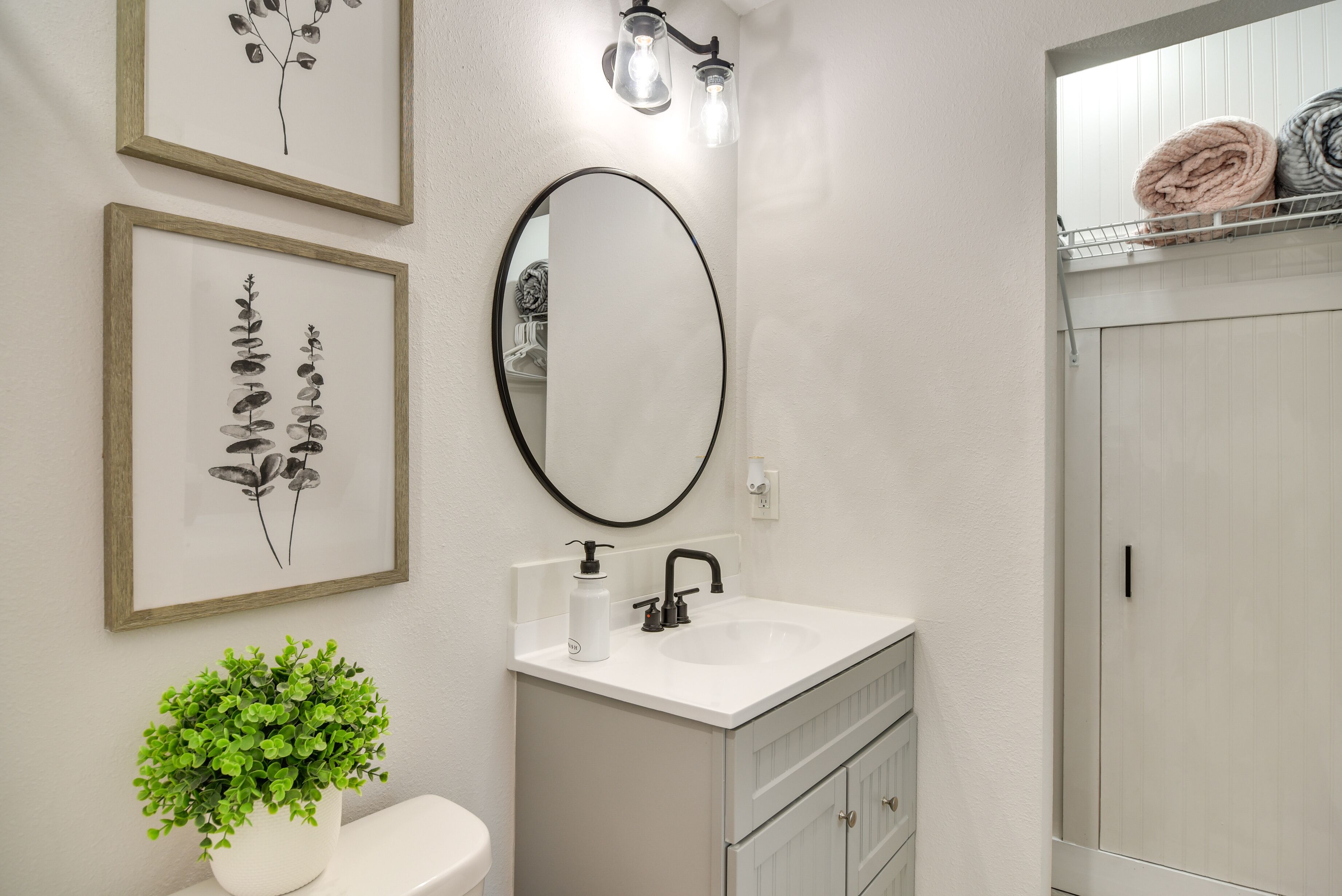 Une salle de bain avec un lavabo blanc, un miroir, des reproductions botaniques encadrées, une plante en pot et un porte-serviettes avec des serviettes.