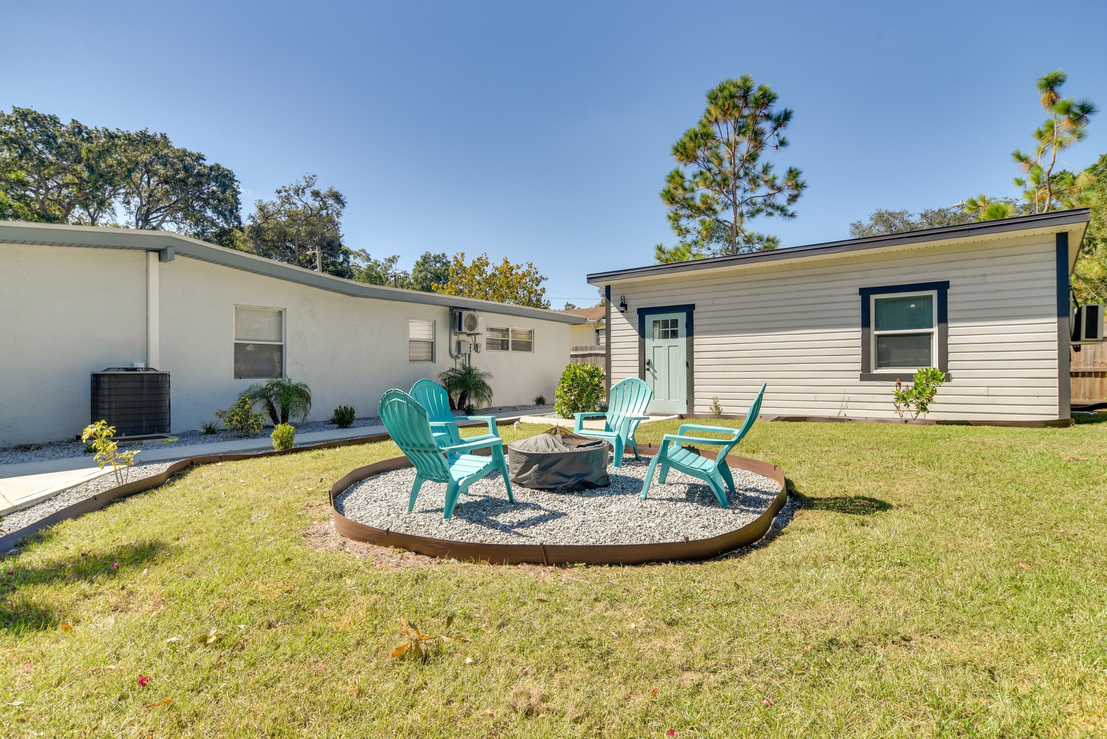 A residential area with a small house, a fire pit with chairs, and a well-maintained lawn.