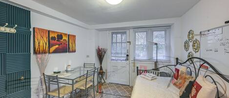 A compact room with a bed, a glass table with chairs, a door, and a window.