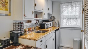 A compact kitchen with white cabinets, a granite countertop, a coffee machine, and a window with lace curtains. - Pet-friendly Great Neck Home ~ 1 Mi to Kings Point (Great Neck)