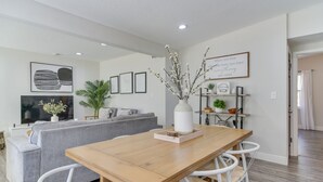 Een moderne woonkamer met een houten eettafel, witte stoelen, een grijze bank en een flatscreen-televisie.