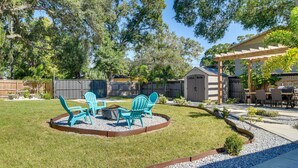 Un jardin avec une pergola en bois, un espace barbecue équipé de chaises et une cour clôturée.