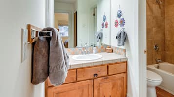 A bathroom with a wooden vanity, a white sink, a mirror, and a shower area.