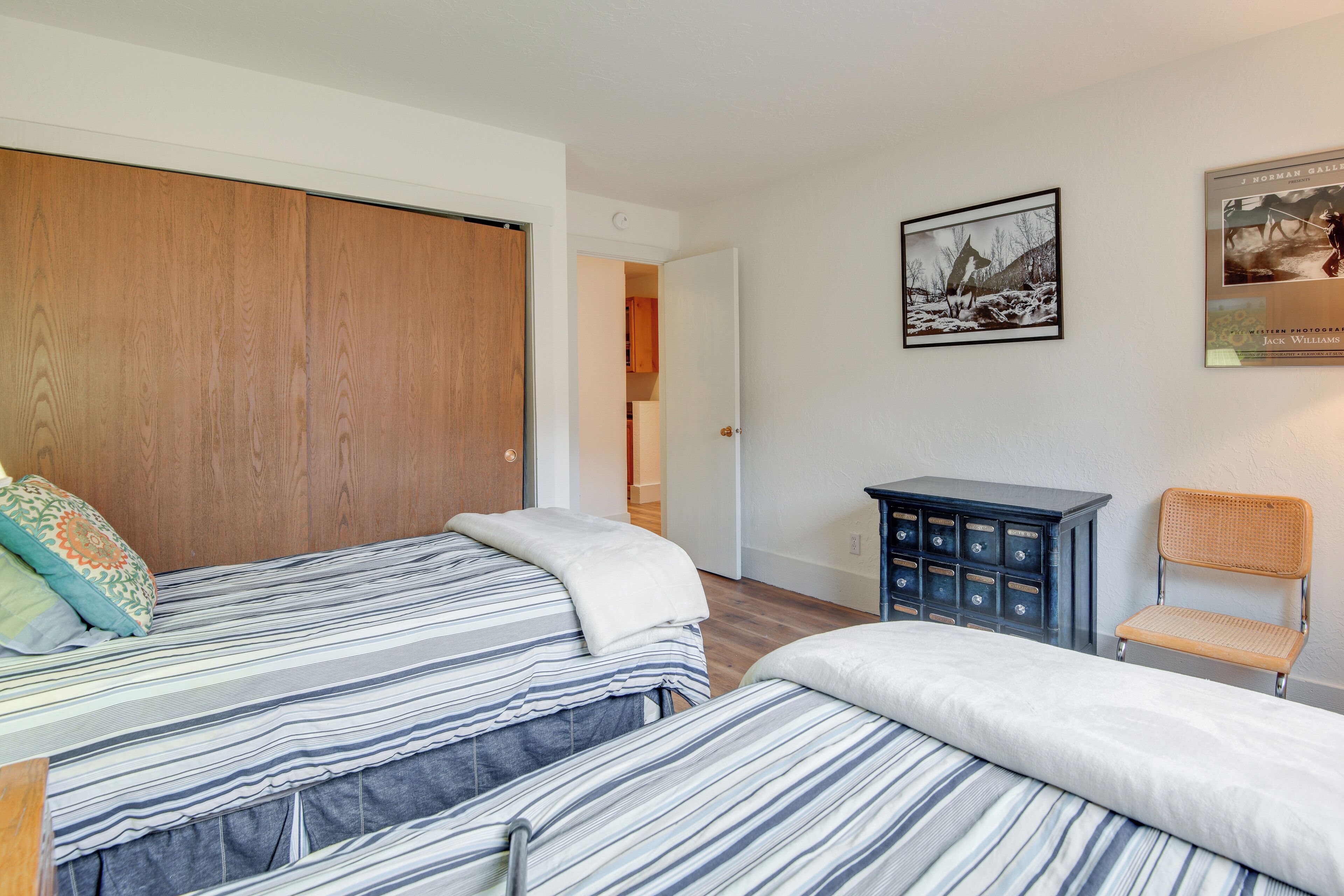 A bedroom with two beds, a wooden wardrobe, a small cabinet, and a chair.