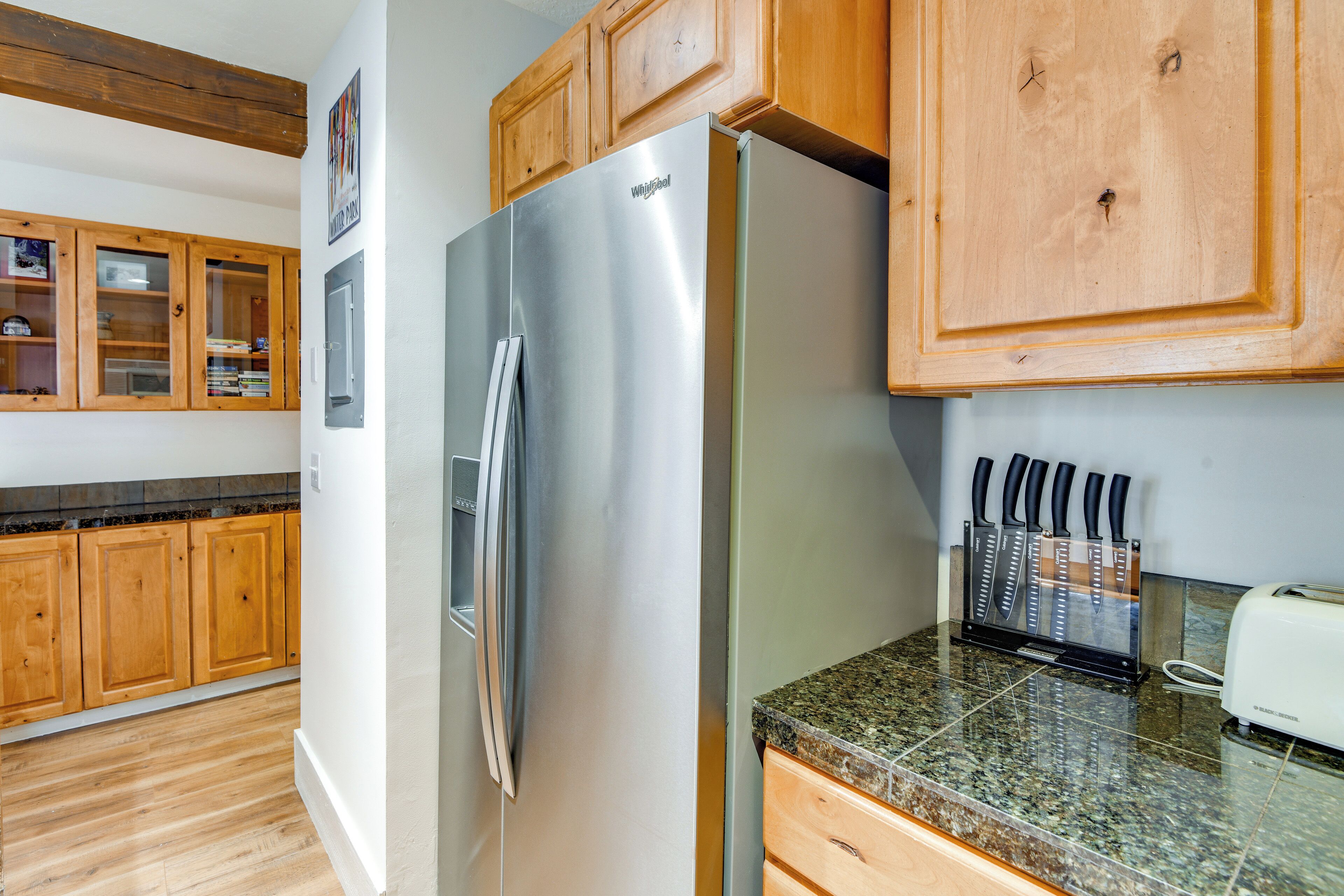 Una cocina con armarios de madera, refrigerador de acero inoxidable, encimeras de granito y un bloque de cuchillos.