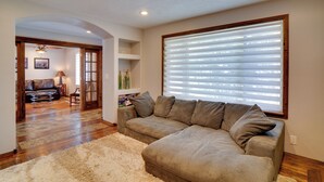 A living room with a sectional sofa, a large window with blinds, a fluffy rug, and a wooden floor. - Kaysville Group Getaway 26 Mi to Snowbasin Resort! (Kaysville)
