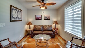A living room with a brown leather sofa, a glass coffee table, and two lamps. There are framed pictures on the wall and a ceiling fan. - Kaysville Group Getaway 26 Mi to Snowbasin Resort! (Kaysville)
