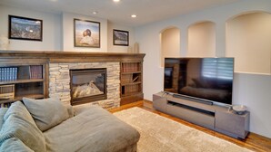 A living room with a stone fireplace, a large flat-screen TV, a sofa, and bookshelves. - Kaysville Group Getaway 26 Mi to Snowbasin Resort! (Kaysville)
