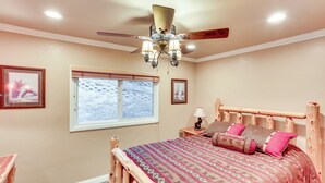 Un dormitorio con cama de madera, ventilador de techo y ventana con vistas a un paisaje nevado.