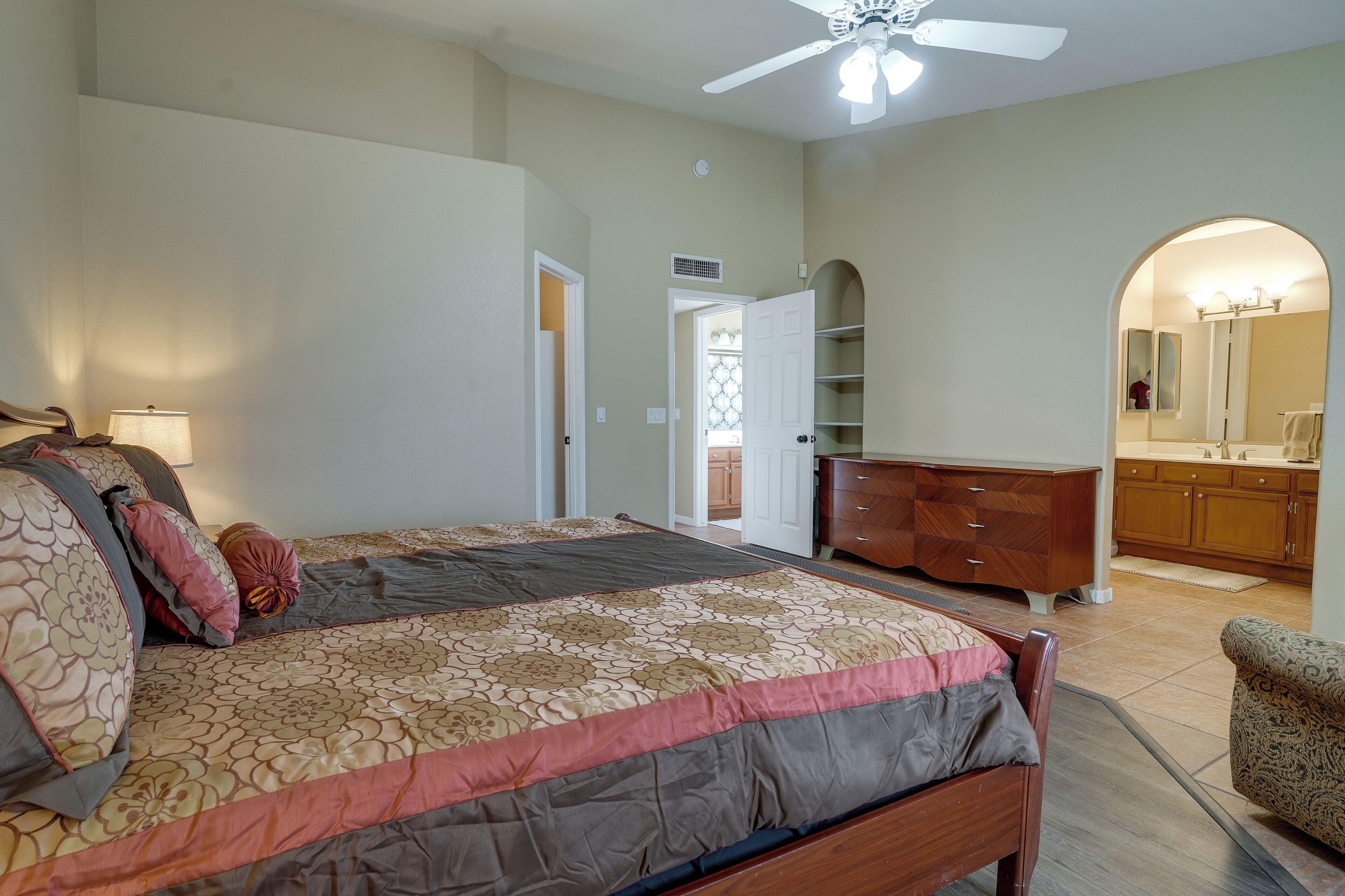 A bedroom with a large bed, a dresser, and a vanity with a mirror.