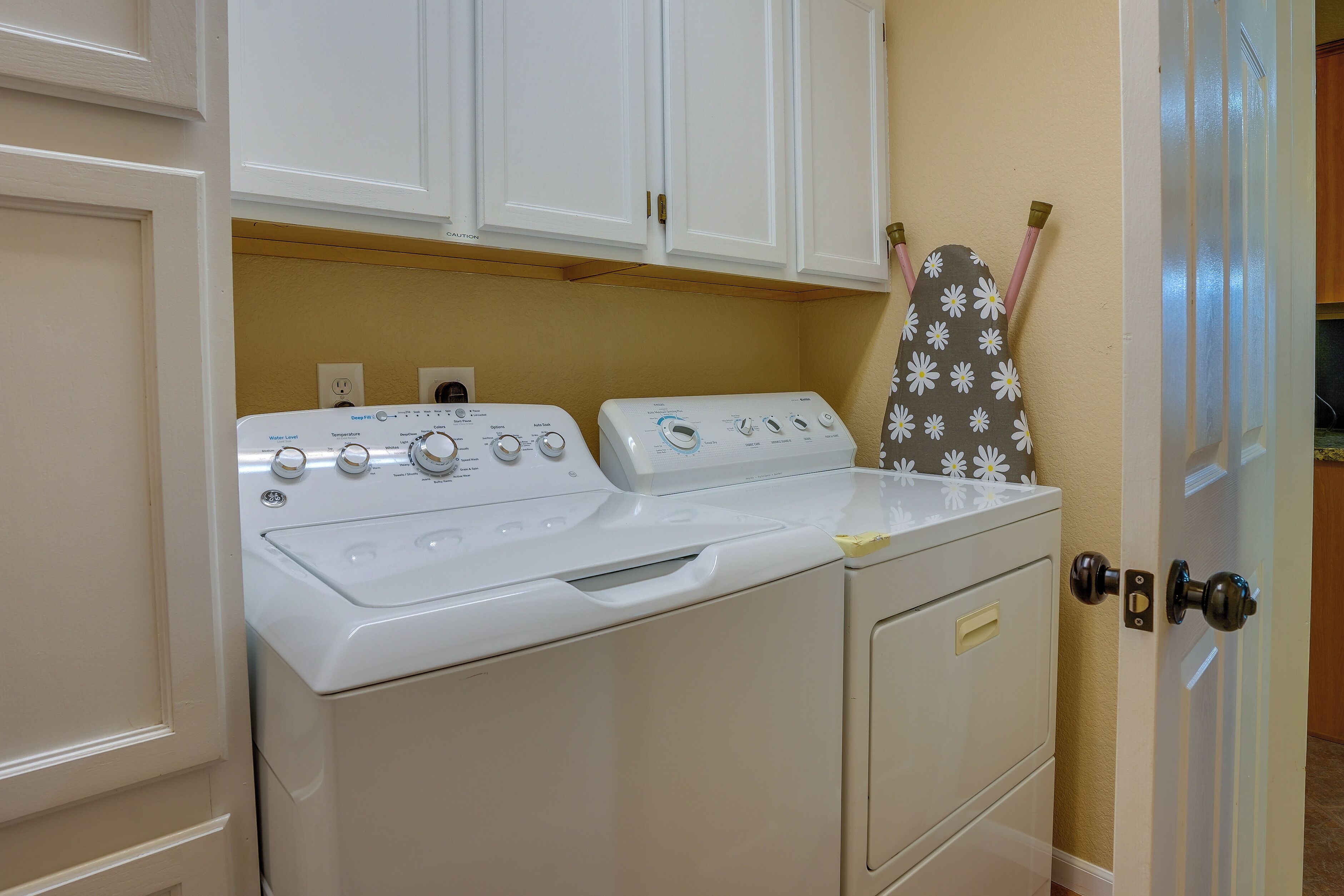 A laundry area with two washers and a dryer, a white door, and a towel rack with a floral pattern.