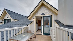 A covered outdoor patio with a glass table and chairs, a white railing, and a door leading to an interior room.