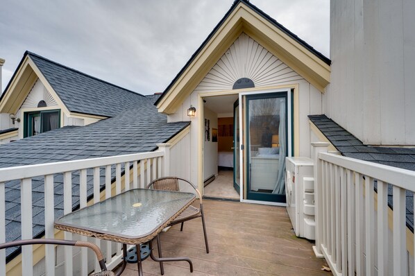 A covered outdoor patio with a glass table and chairs, a white railing, and a door leading to an interior room.