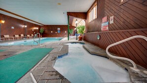 An indoor swimming pool with a wooden interior, a hot tub, and a staircase leading to an upper level.