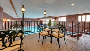 An indoor patio area with a pool, furnished with tables and chairs, and a railing around the pool.