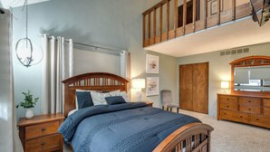 Een slaapkamer met een houten bed, nachtkastjes, een dressoir, een stoel en een vide met houten leuning.