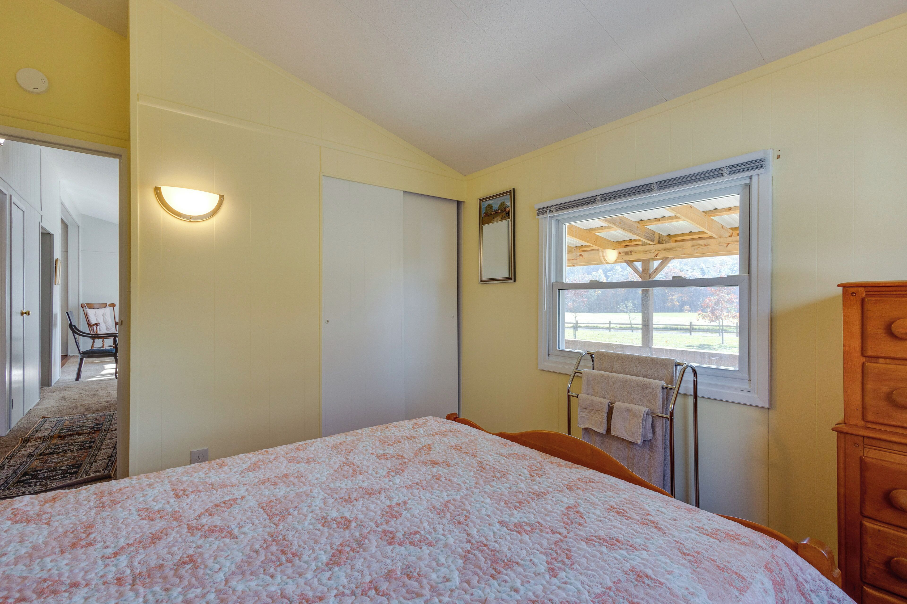 Ein Schlafzimmer mit einem Bett, einer Holzkommode, einem Fenster mit Aussicht, einer Tür und einem Stuhl.