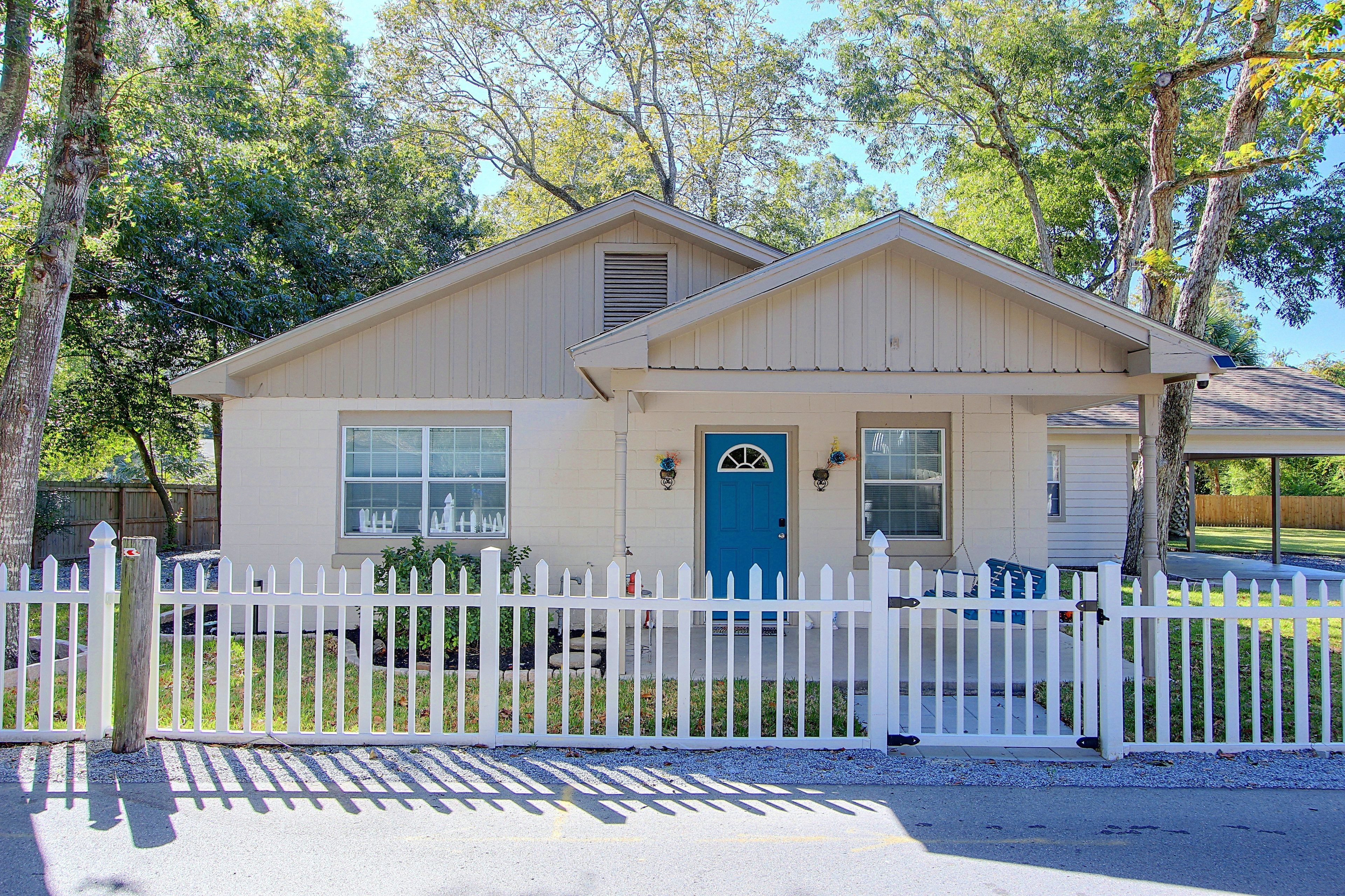 A single-story house with a white picket fence, a blue front door, and a small porch with a bench.