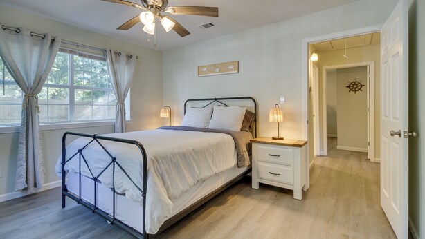 A bedroom with a bed, bedside tables, a ceiling fan, and a door leading to another room. - Ample Trailer/rv Parking! Family Home in Gulfport (Gulfport)