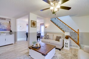 A spacious living room with a high ceiling fan, a staircase, a white sofa, and a dining area with a white cabinet. - Pet-friendly Cottage: 8 Mi to Paul Bunyan Land! (Brainerd)
