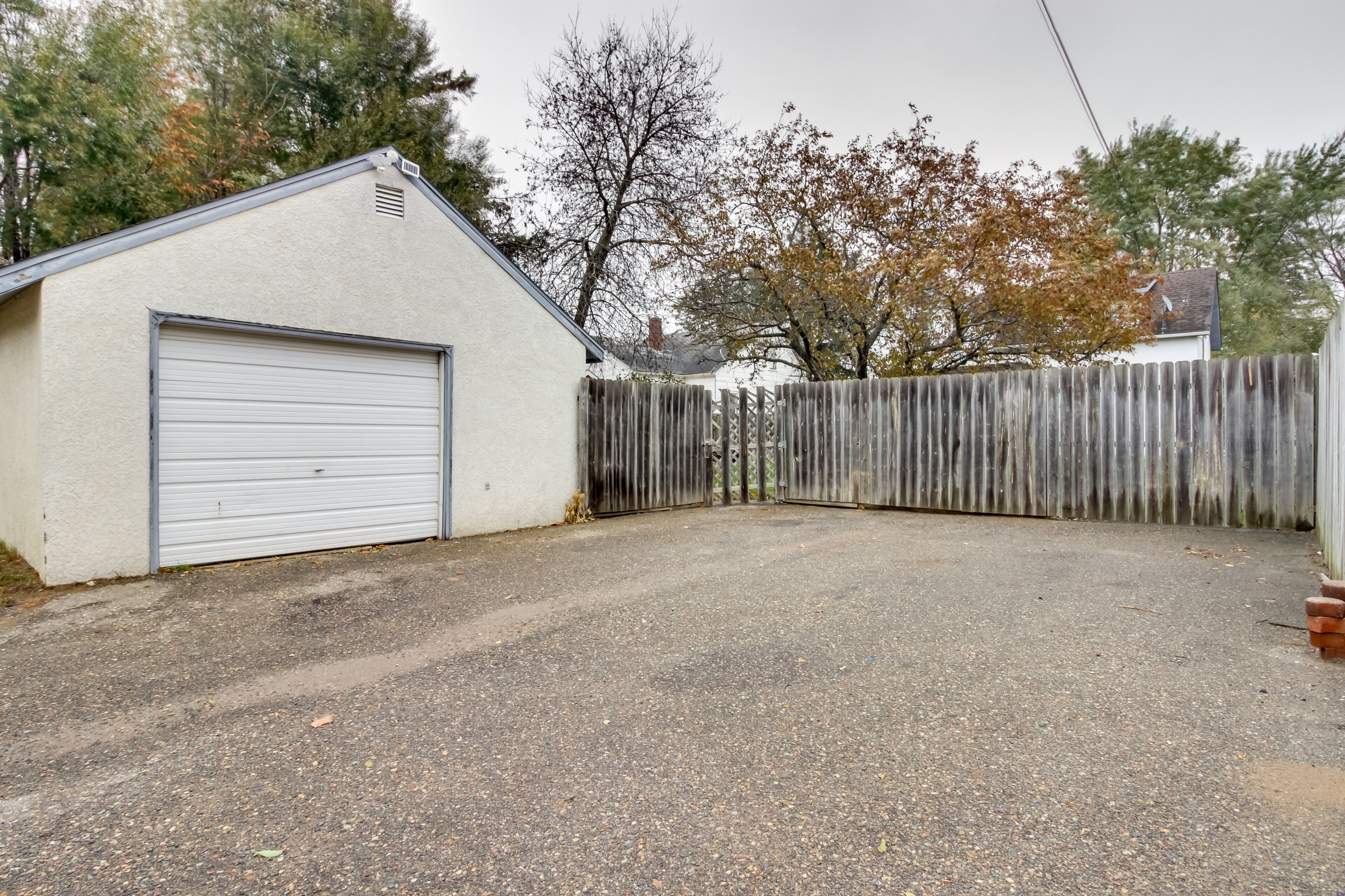 A garage with a closed white door, a gravel driveway, and a wooden fence.